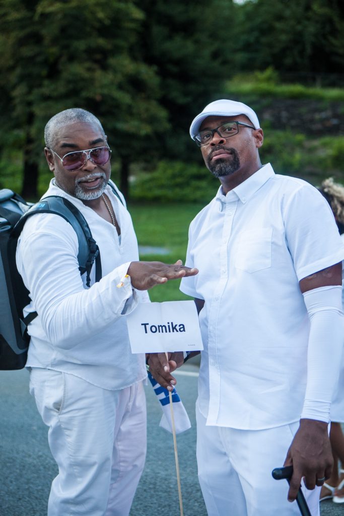 Brown men holding sign at Diner En Blanc