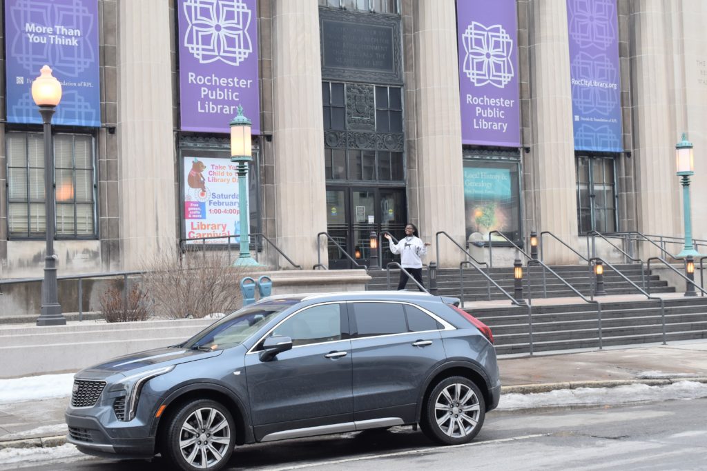 brown skin girl in front of Rochester public library with Cadillac XT5