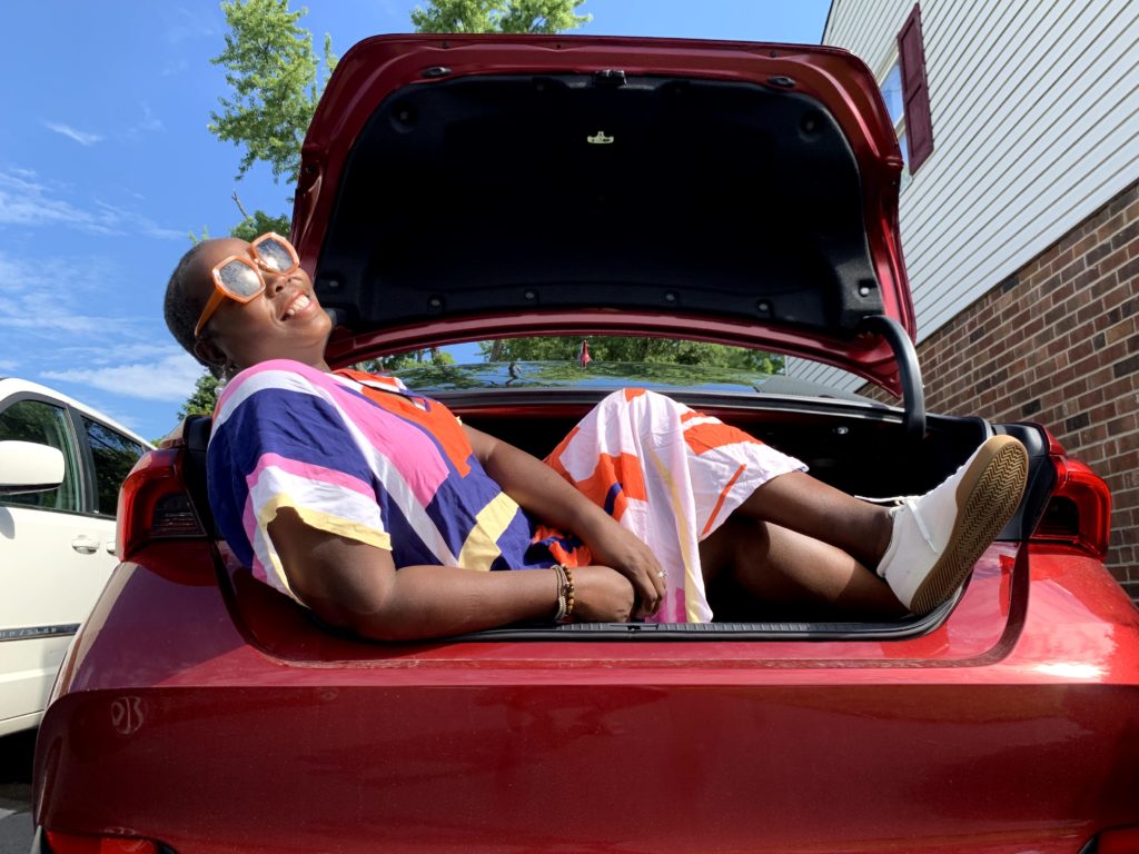 brown girl wearing kaftan with Roth's sneakers in trunk of 2021 Toyota Avalon hybrid